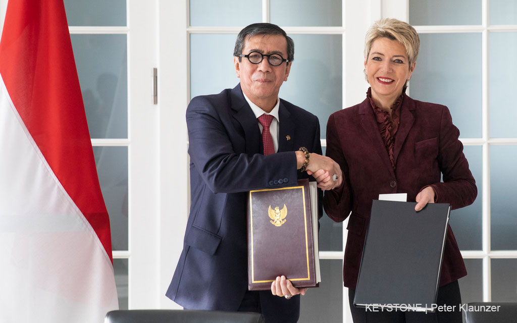La conseillère fédérale Karin Keller-Sutter et le ministre indonésien de la Justice et des droits de l’homme Yasonna Laoly, chacun avec un exemplaire du traité signé, échangent une poignée de mains.